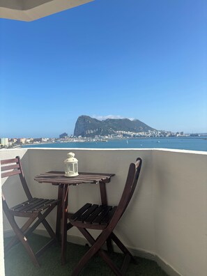 A balcony with a table and chairs, overlooking a coastal cityscape with a prominent mountain. - Studio with terrace and spectacular views (La Línea de la Concepción)
