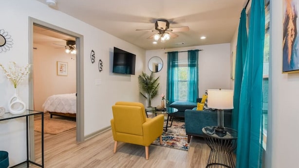 Un salon moderne avec un canapé, un fauteuil jaune, un téléviseur et un ventilateur de plafond.