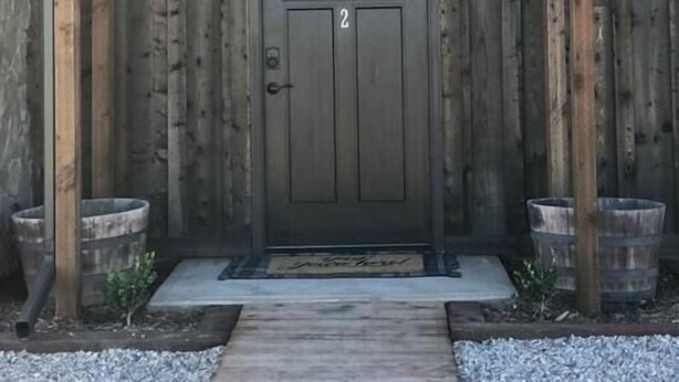 Ein Holzgebäude mit einer dunkelbraunen Tür, zwei kleinen Fenstern und zwei Wandleuchten.
