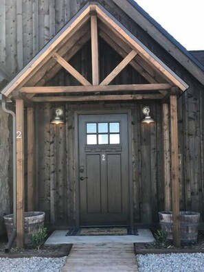 A wooden building with a dark brown door, two small windows, and two wall-mounted lights.