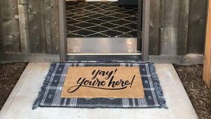 Eine Holztür mit Glasschieber, eine schwarz-weiße Fußmatte und ein Schild mit der Aufschrift 'yay! you're here!'