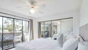 Een slaapkamer met een groot bed, een plafondventilator en een schuifdeur naar een buitenruimte.