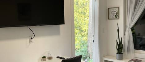 En moderne stue med et fladskærms-tv på væggen, en sort kontorstol, et lille bord med en plante og en bænk med en bog.