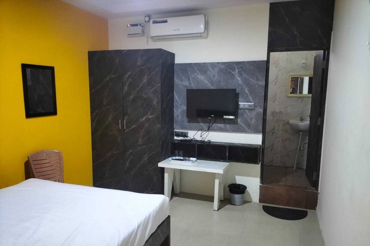 A hotel room with a bed, a desk, a television, a mirror, and a bathroom with a sink and toilet.