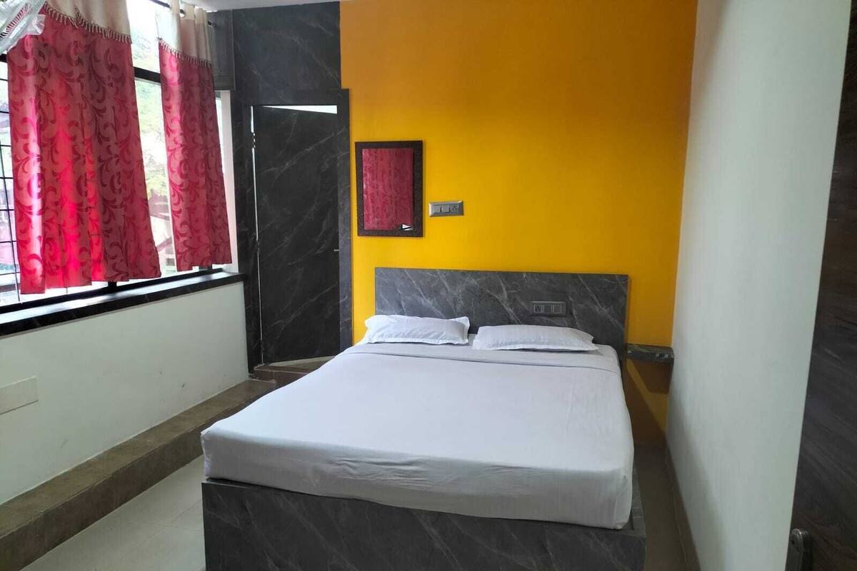 A bedroom with a bed, a window with curtains, a door, and a wall with a picture.
