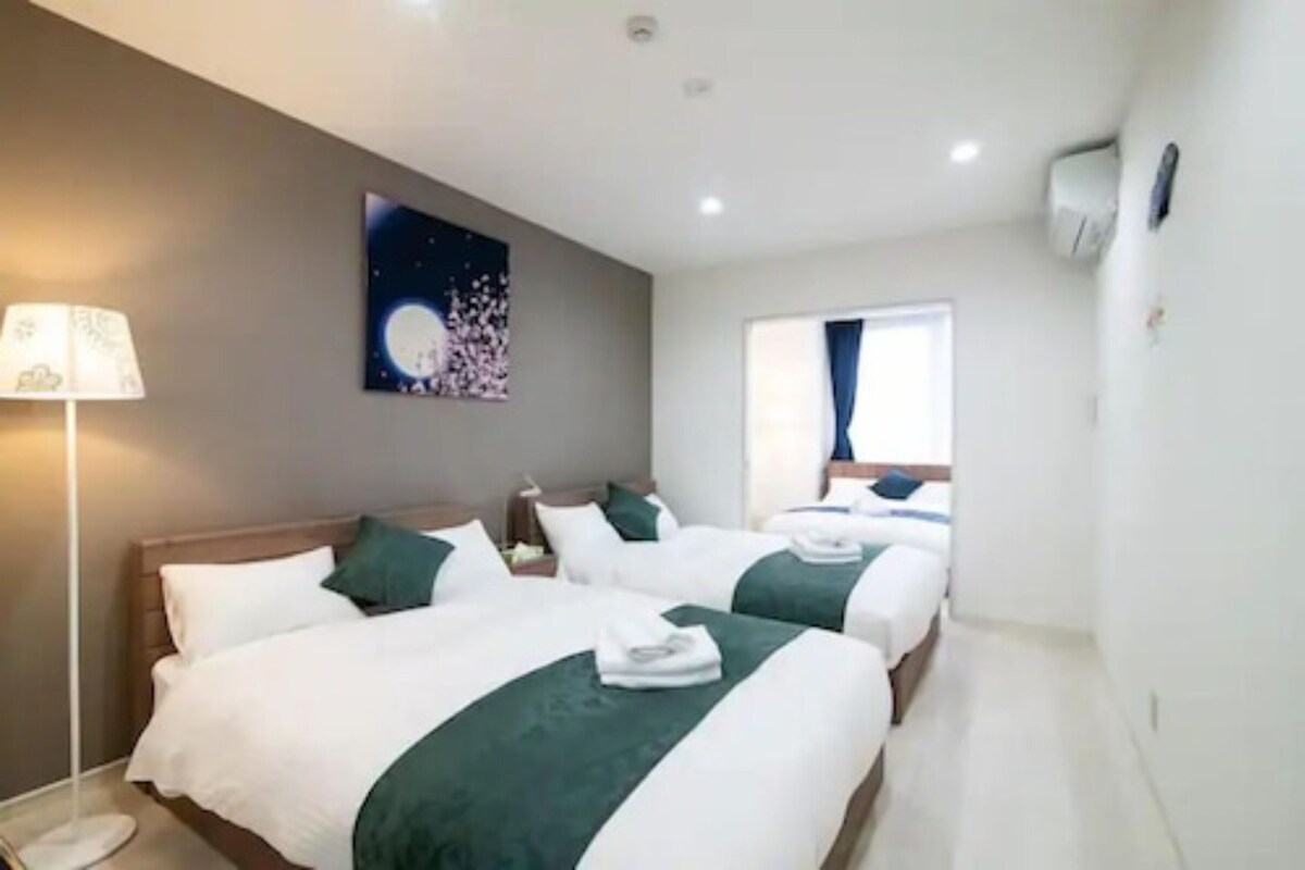 Una habitación de hotel con dos camas, una mesita de noche, una lámpara, un cuadro y una ventana con cortinas.