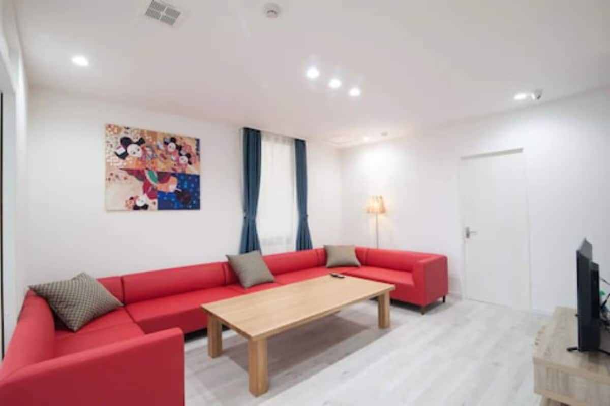 A modern living room with a red sectional sofa, a wooden coffee table, and a flat-screen TV on a wooden stand.