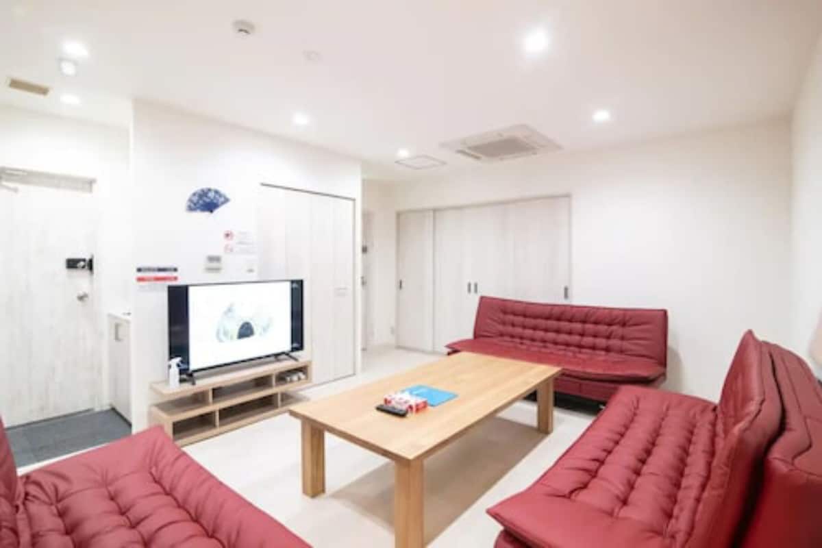 A room with a wooden table, red sofas, a flat-screen TV, and white walls.