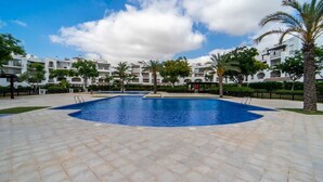 A swimming pool with a tiled deck, surrounded by buildings with balconies and palm trees.