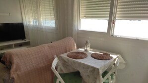 A room with a bed, a table with two woven placemats, a green chair, a white tablecloth, a white lamp, and a television on a stand. - Loft con Espectaculares Vistas al Mar, Gibraltar, Marruecos y Bahía de Algeciras (La Línea de la Concepción)