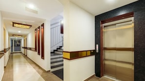 A hotel corridor with a staircase, an elevator, and a hallway leading to another room. - Hotel Burooj (Kanayannur)