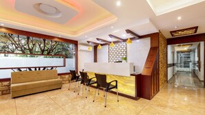 A reception area with a sofa, chairs, a reception desk, and a decorative wall. - Hotel Burooj (Kanayannur)