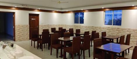A dining area with multiple tables and chairs, a buffet setup on the left, and a stone wall with a window on the right.