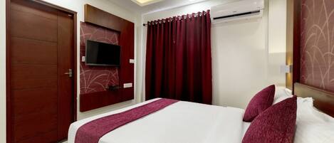 A hotel room with a bed, a TV mounted on the wall, and an air conditioning unit.