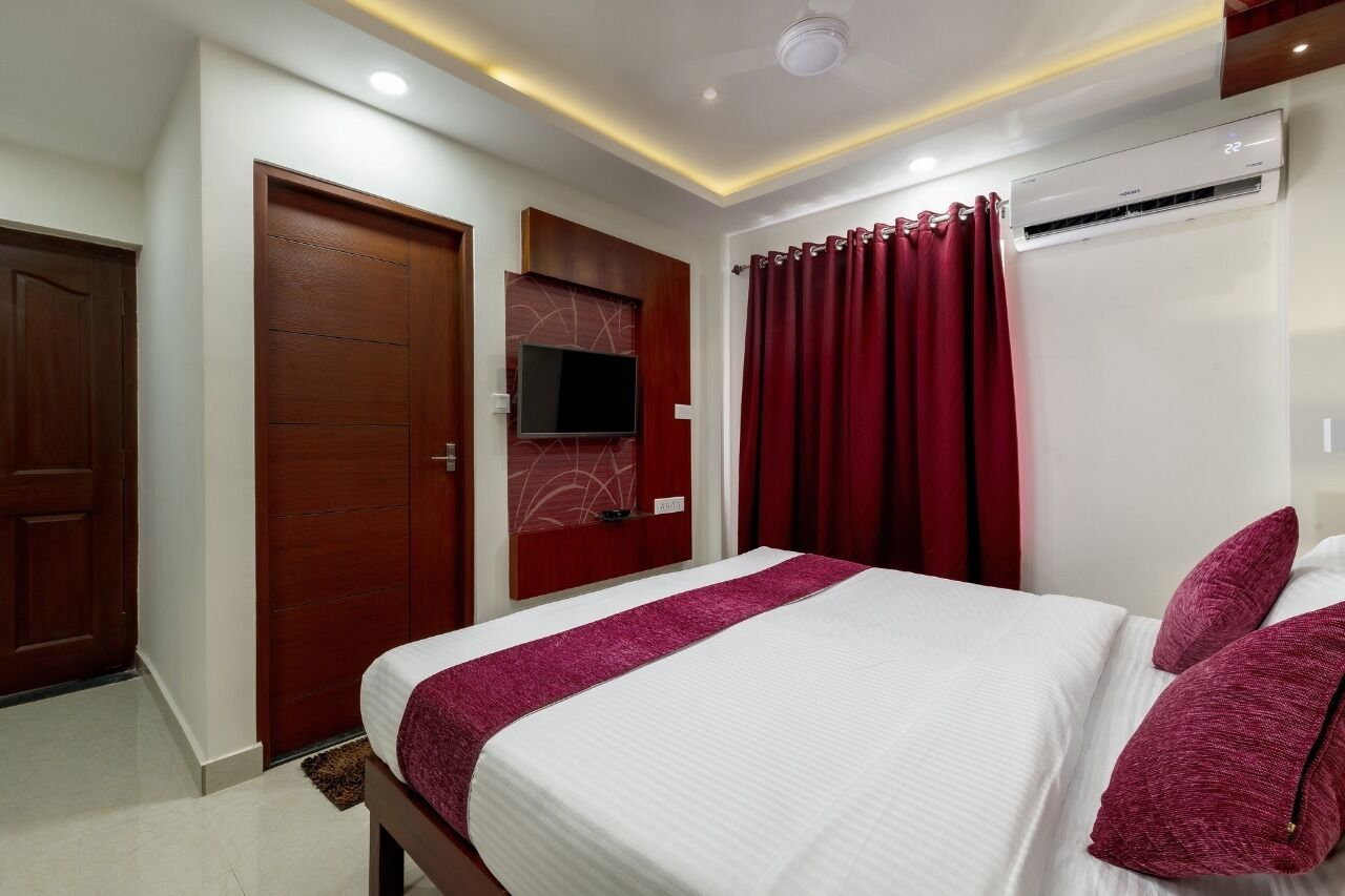 Una habitación de hotel con cama, televisor montado en la pared, armario de madera y cortina roja.