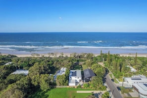An aerial view of a coastal residential area with houses, a beach, and a clear blue sky.