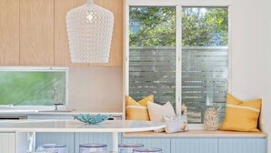 Une cuisine dotée d’une grande fenêtre, d’un luminaire suspendu et d’un îlot central intégré avec des tabourets.
