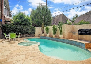 A backyard with a swimming pool, stone patio, green chairs, and potted plants.