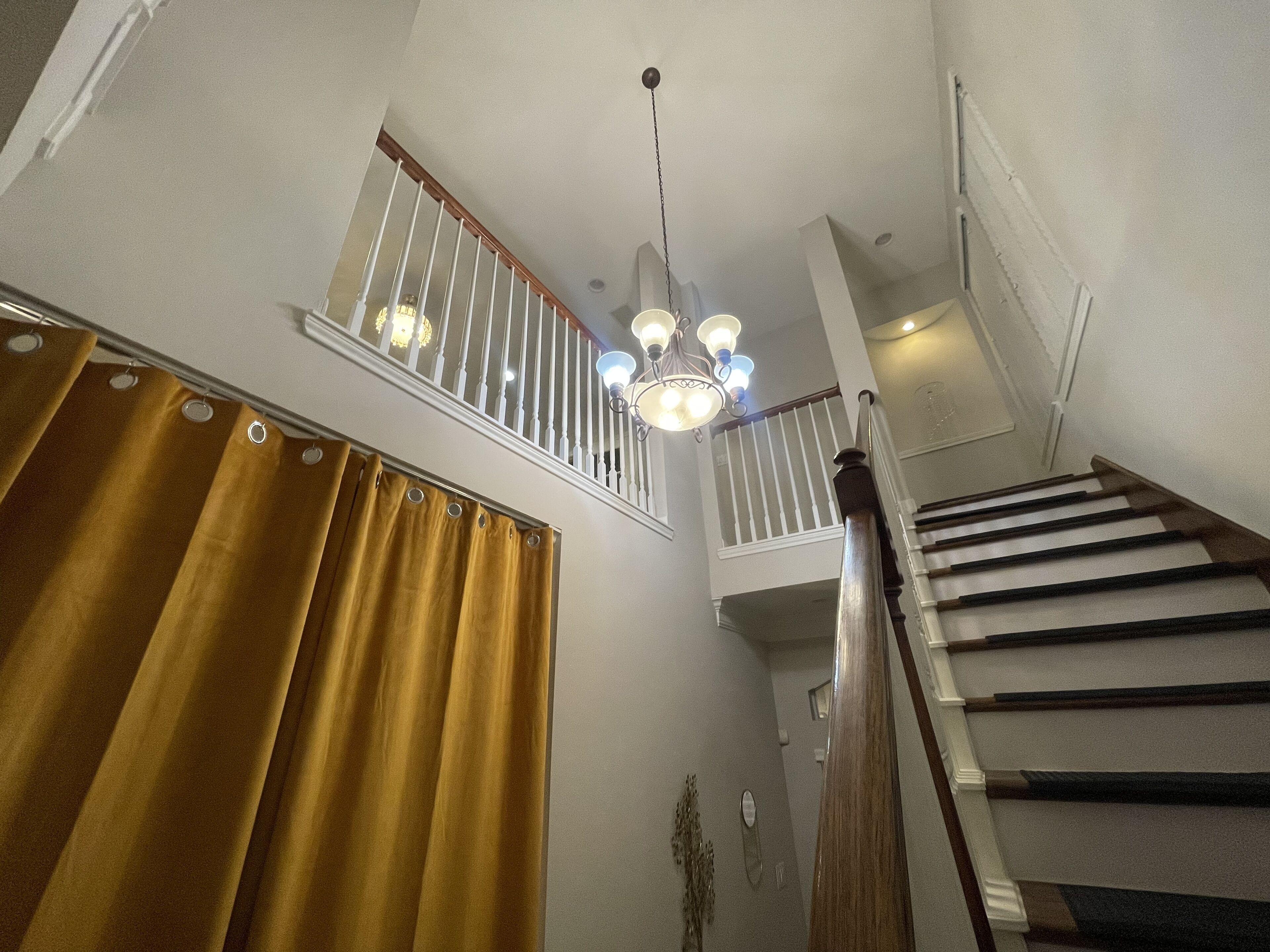 Eine Treppe mit hölzernem Handlauf und weißen Spindeln, die zu einer Empfangshalle im zweiten Stock mit einem Chandelier führt.