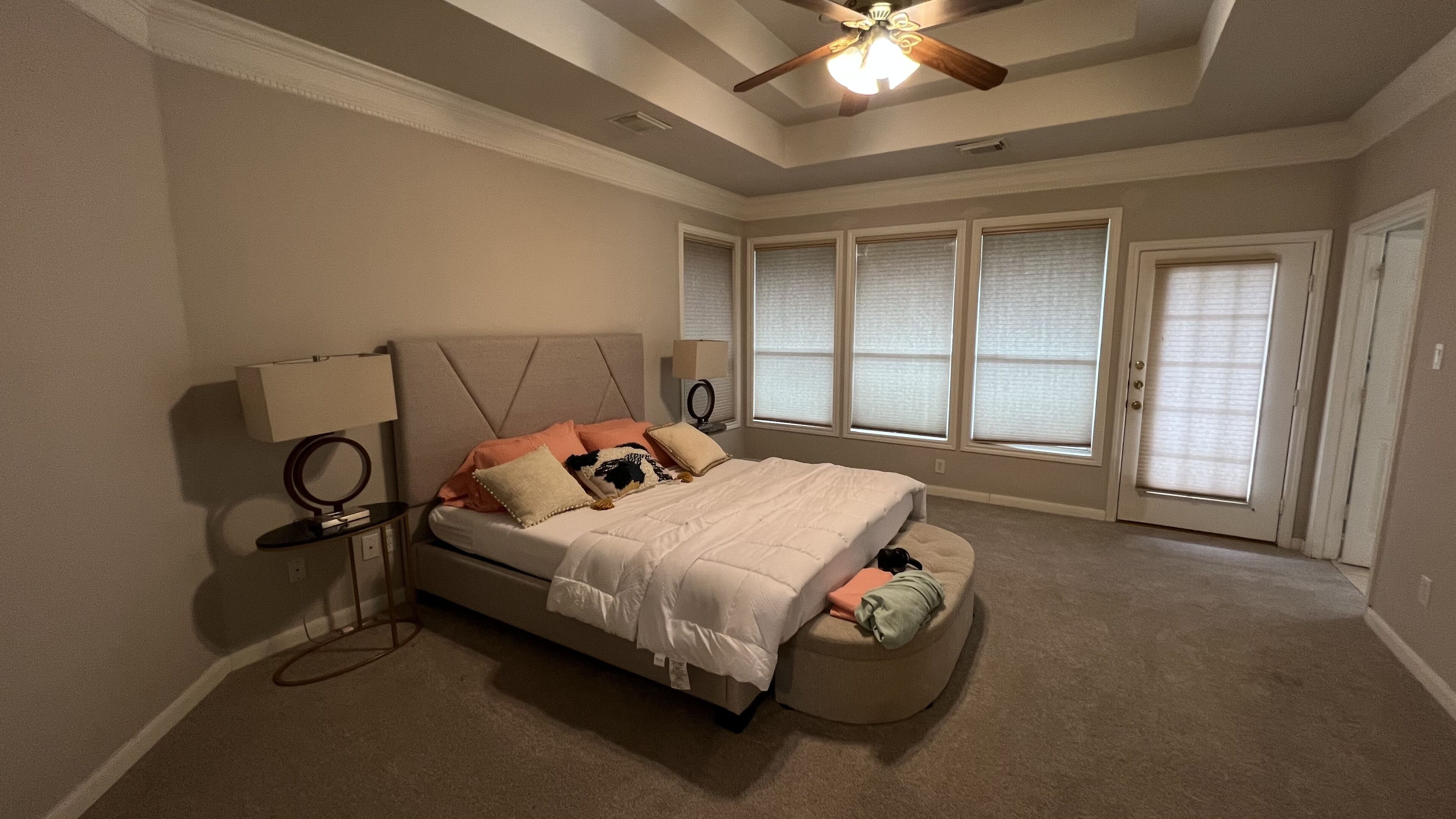 A bedroom with a bed, bedside tables, a ceiling fan, and large windows with blinds.