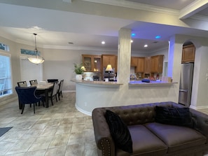 A modern kitchen with a central island, a dining area with chairs, and a leather sofa.