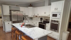 A modern kitchen with white cabinets, stainless steel appliances, and a marble island with bar stools. - Jacksonville Ranch with private Hottub and Pool, stocked Pond with row boat, Bike and Hiking trails (Maysville)