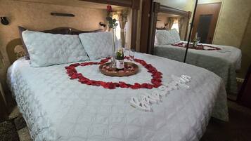 Een tweepersoonsbed met een hartvormige bloemopstelling van rode rozenblaadjes en een fles champagne.
