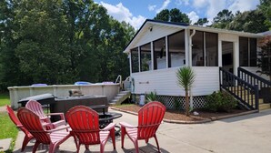 A covered outdoor area with a fire pit, red Adirondack chairs, and a white building with a porch. - Jacksonville Ranch with private Hottub and Pool, stocked Pond with row boat, Bike and Hiking trails (Maysville)