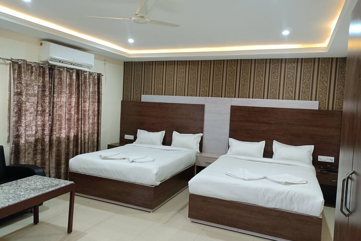 Quarto de hotel com duas camas, uma escrivaninha, ventoinha no teto e um painel decorativo na parede.