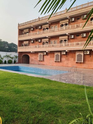 A multi-story building with a swimming pool and a grassy area in front.