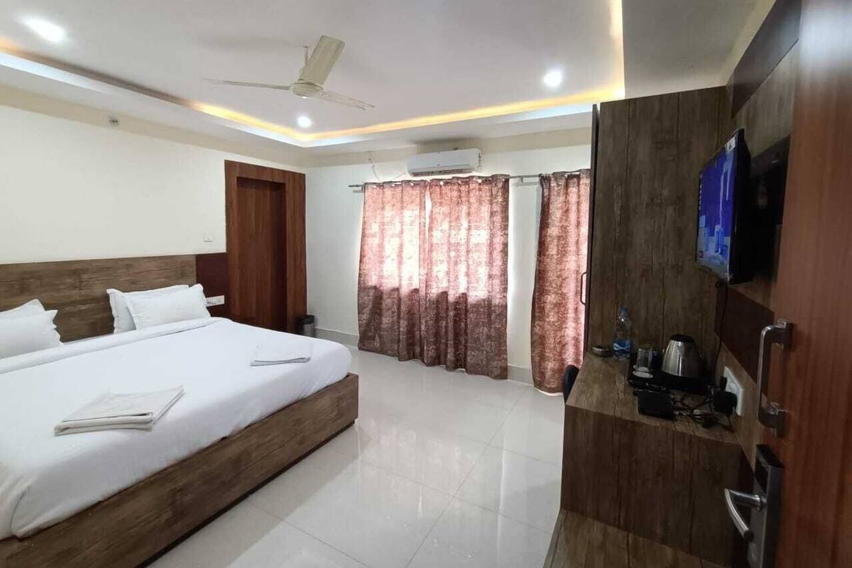 Quarto de hotel com uma cama grande, televisão, guarda-roupa e ventoinha no teto.