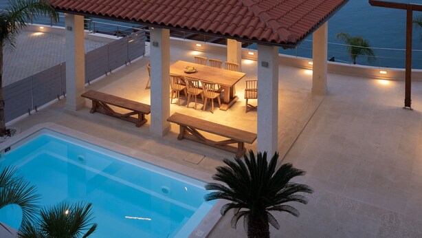 Un espace extérieur abrité, aménagé pour les repas, avec une piscine et une vue sur la mer.
