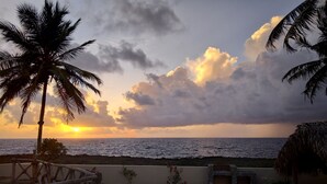 Ein Poolbereich mit Blick auf das Meer bei Sonnenuntergang, Palmen und eine Steinmauer.