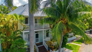A two-story house with a white exterior, a front porch, and a fenced yard with palm trees. - Doc`s Paradise (Key West)