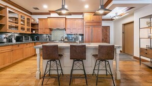 Une cuisine moderne avec des meubles en bois, un îlot central doté de tabourets de bar et un éclairage suspendu.