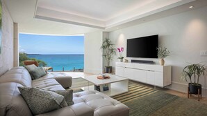Een moderne woonkamer met een witte bank, een salontafel en een flatscreen-tv. Er staan potplanten en is uitzicht op zee.