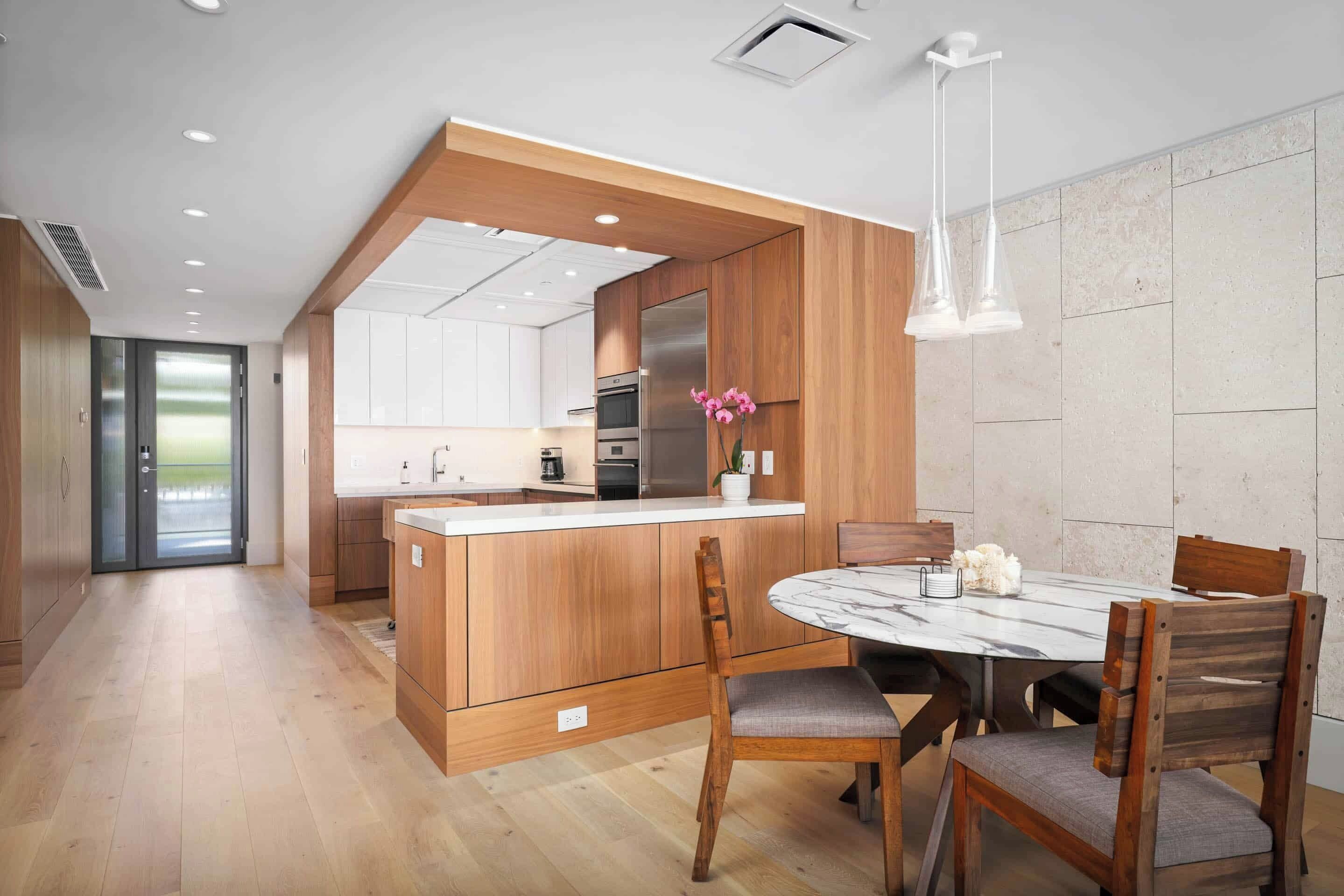 Eine moderne Küche mit Holzschränken, einer zentralen Kochinsel und einem Essbereich mit Marmortisch und Holzstühlen.