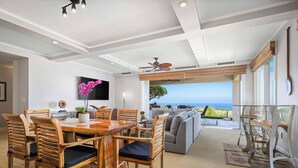 A modern living room with a dining area, a large TV, and a view of the ocean. - Wai'ula'ula C102 Three Bedroom (Kamuela)