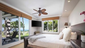 A bedroom with a bed, a ceiling fan, a TV, and a view of the outdoors. - Wai'ula'ula C102 Three Bedroom (Kamuela)