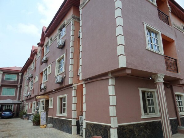 A multi-story building with a pink facade and white trim. There are multiple windows on each floor, and the building has a balcony on the upper floors. - Hardrock Hotel and Suites Ltd (Lagos)