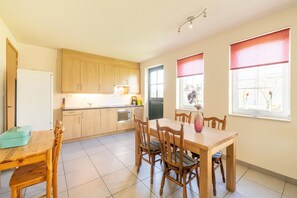A modern kitchen with wooden cabinets, a dining table with chairs, and a refrigerator. - Holiday home in Sint Kruis with a garden (Sint Kruis)