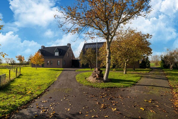 A brick building with a sloped roof, a paved driveway, and a grassy area with trees. - Holiday home in Sint Kruis with a garden (Sint Kruis)
