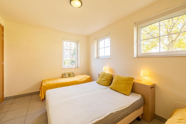A bedroom with two beds, a window, and a bedside lamp.