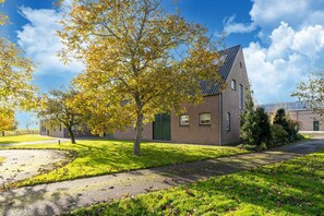 A brick building with a green door, surrounded by a grassy area and trees with yellow leaves. - Holiday home in Sint Kruis with a garden (Sint Kruis)