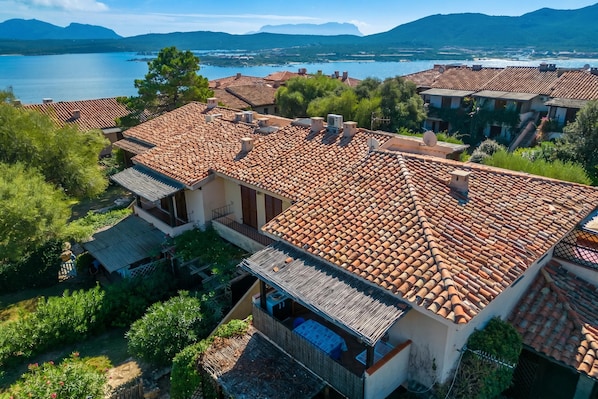 A residential area with terracotta-tiled roofs, a view of a lake, and surrounding greenery. - Casa Emozione With Shared Pool (Olbia)