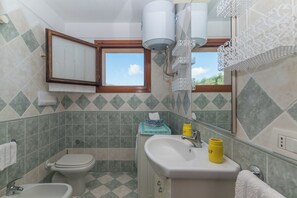 A bathroom with a toilet, sink, and mirror. There is a window with a view of greenery outside. - Casa Emozione With Shared Pool (Olbia)