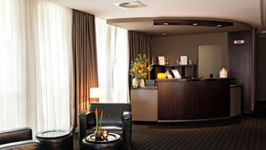 A hotel lobby with a reception desk, a seating area with chairs and a coffee table, and a large window with curtains. - Boston Apartments HH (Hamburg)