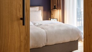 A modern bedroom with a bed, a nightstand, a lamp, and a view of the outside through a window with curtains. - Boston Apartments HH (Hamburg)