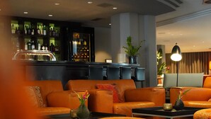 A modern lounge area with orange sofas, a bar in the background, and a patterned ottoman. - Boston Apartments HH (Hamburg)