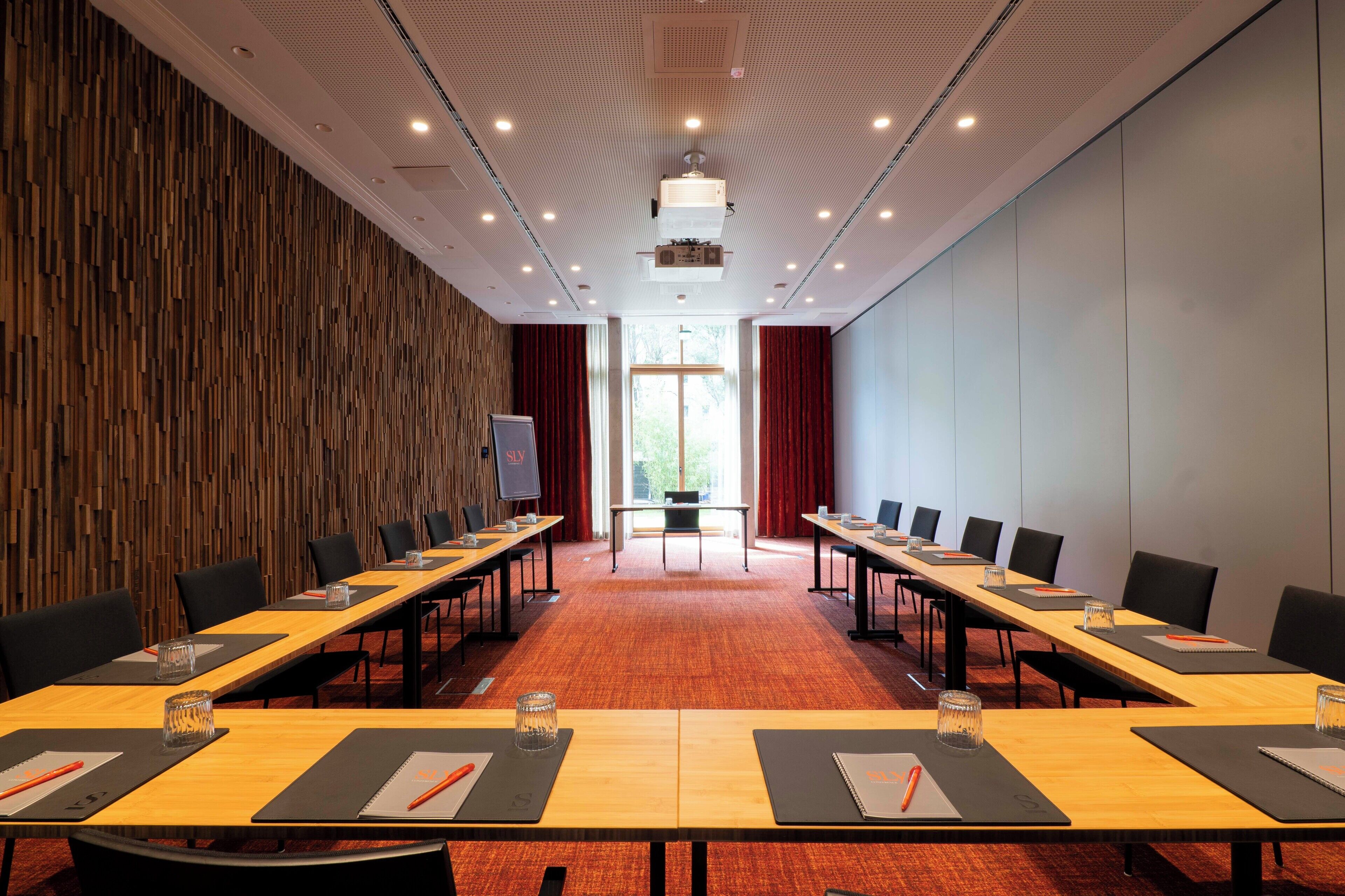Un salón de conferencias con una larga mesa, sillas y una pantalla para proyector.
